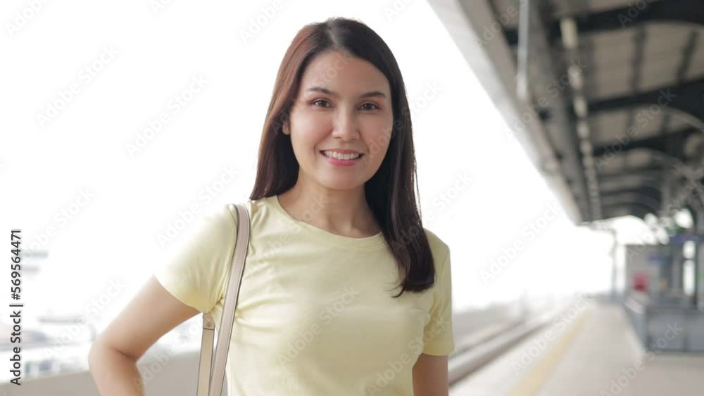 Portrait of beautiful smiling Asian woman standing on platform waiting for electric train in the morning and holding a smartphone. The concept of traffic and capital transportation