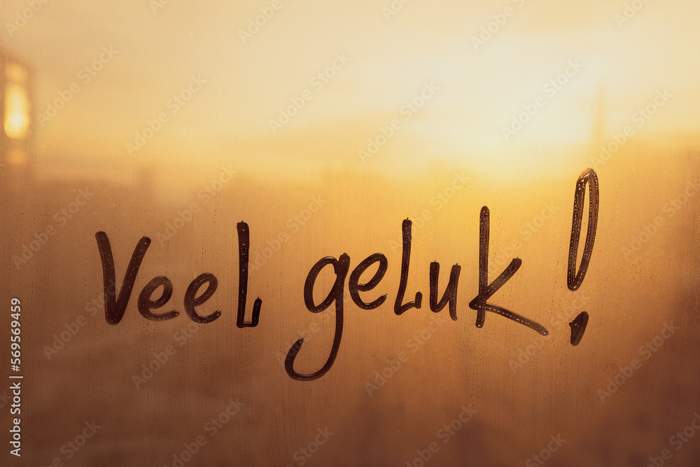 Fototapeta premium Lettering Netherlandish language text Veel geluk is Good luck in english message written finger on foggy glass wet sunset window