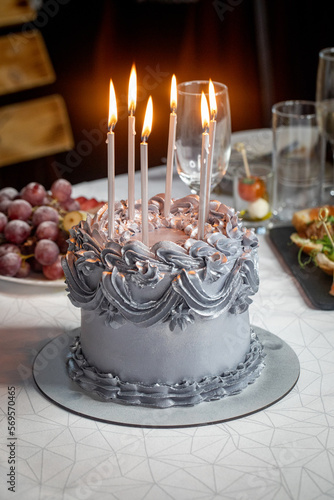 Beautiful silver cake with cream and a 6 burning candles is on the table  a childrens birthday  vertical photo  selective focus.
