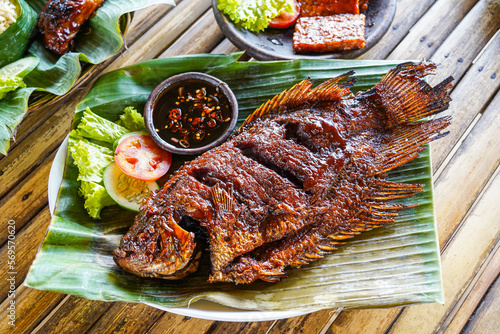 Grilled gurami or grilled gurame with red barbecue sauce, vegetables and chili sauce served on banana leaves, photo