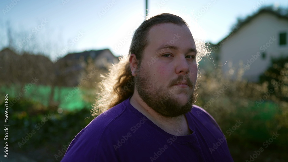 Portrait of a young casual caucasian overweight man standing outside looking at camera with serious expression Portrait of a young casual caucasian overweight man standing outside looking at camera with serious expression