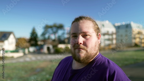 Portrait of a happy overweight young man standing outside looking at camera. One casual male person with beard smiling