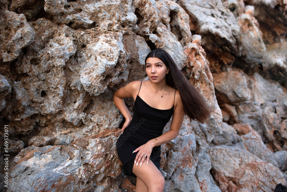 Beautiful brunette in a black dress posing near the rocks and the sea. Attractive brunette woman in a little black dress on the sea coast. Beautiful brunette in a black dress posing near the rocks and the sea. Attractive brunette woman in a little black dress on the sea coast.