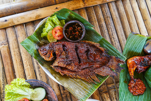 Grilled gurami or grilled gurame with red barbecue sauce, vegetables and chili sauce served on banana leaves, photo