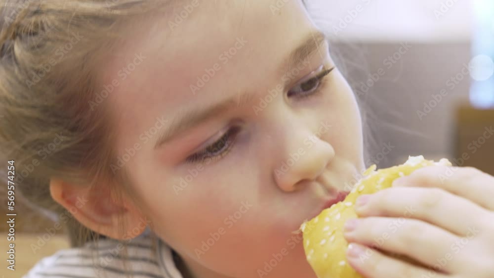 a cute little girl eats a burger in a cafe. the concept of fast food. harmful and tasty snack for children and adults.