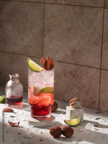 Refreshing cocktail with red syrop or liquer lime,lychee and tonic on marble podium in front of tile,pink background in sunny light.Close up of drink.