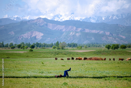 Kyrgyzstan  March 2022  A young man is resting lying on the grass  with mountain ranges in the background.