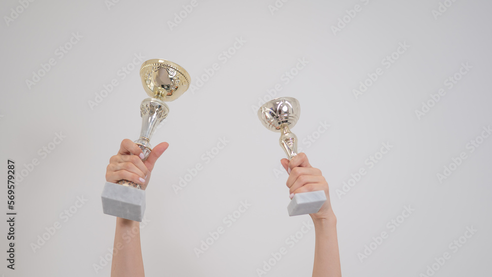 Two golden trophy cups in female hands on a white background. Two golden trophy cups in female hands on a white background.