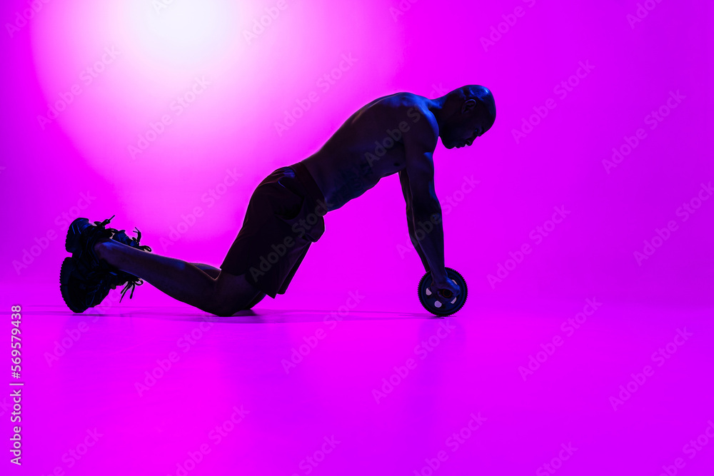 Bodybuilder working on his abs with a ab roller on studio background