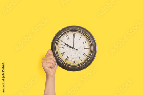 Mano de mujer sosteniendo un reloj sobre un fondo amarillo liso y aislado. Vista de frente y de cerca. Copy space