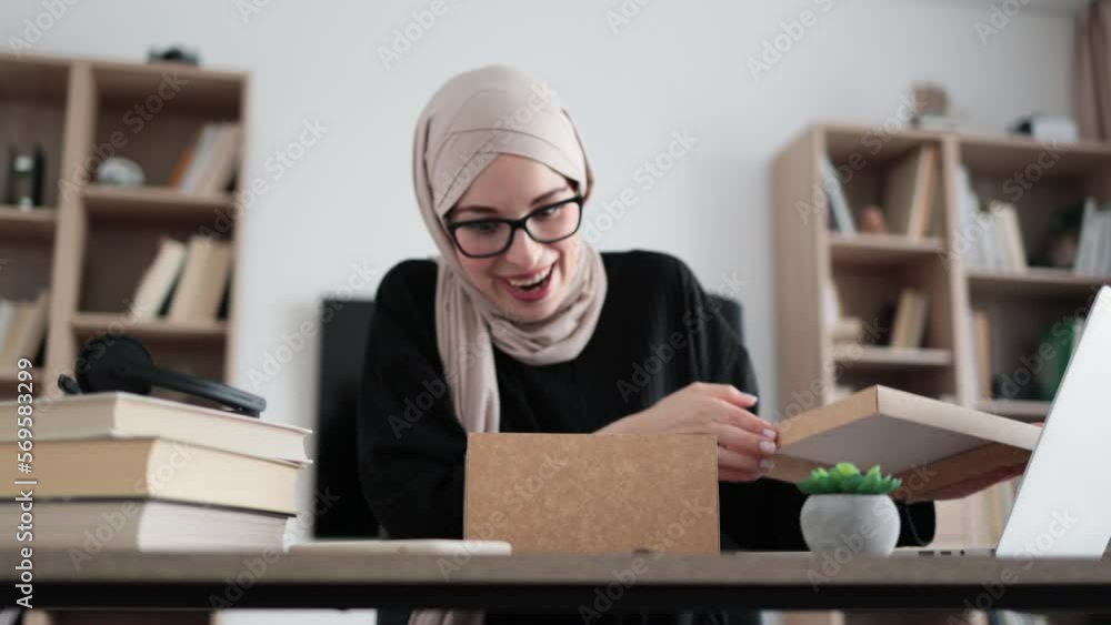 First person view of muslim female blogger opening gift box while sitting at home. Positive young woman doing live stream during unpacking process. First person view of muslim female blogger opening gift box while sitting at home. Positive young woman doing live stream during unpacking process.