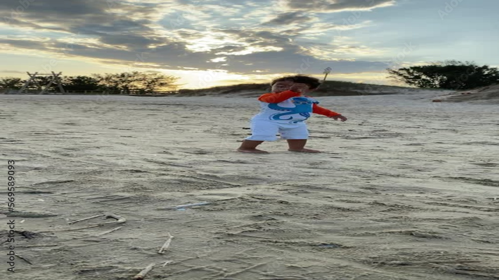 Boy running and having fun on the beach smiling amid sand, dunes and windy trees on a late afternoon sunset with shades of orange and gray clouds. Mention happiness and discoveries. Boy running and having fun on the beach smiling amid sand, dunes and windy trees on a late afternoon sunset with shades of orange and gray clouds. Mention happiness and discoveries.