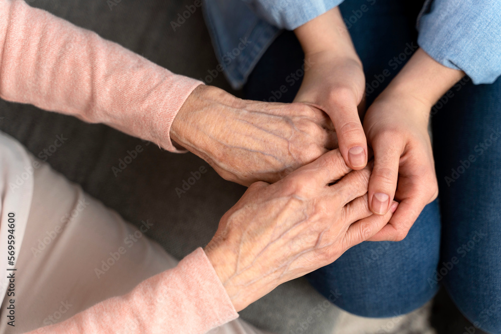 Top view of the mature female aged wrinkled skin and hands of her care giver. Senior woman in elderly care facility gets help from hospital personnel nurse. Grand mother everyday life concept Top view of the mature female aged wrinkled skin and hands of her care giver. Senior woman in elderly care facility gets help from hospital personnel nurse. Grand mother everyday life concept