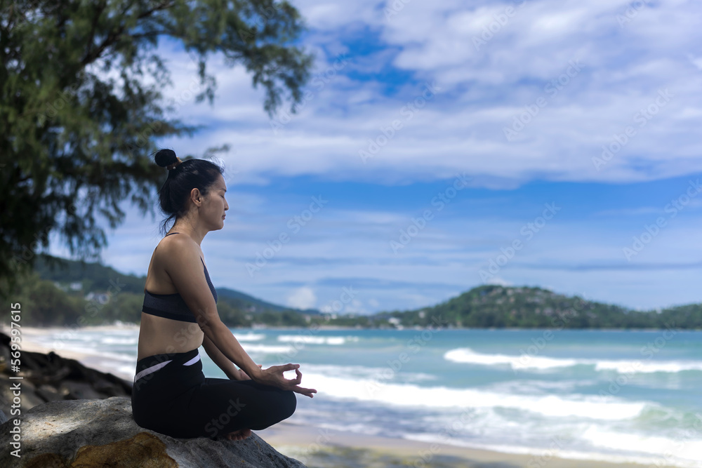 Asian woman sitting on rock doing Yoga on beach