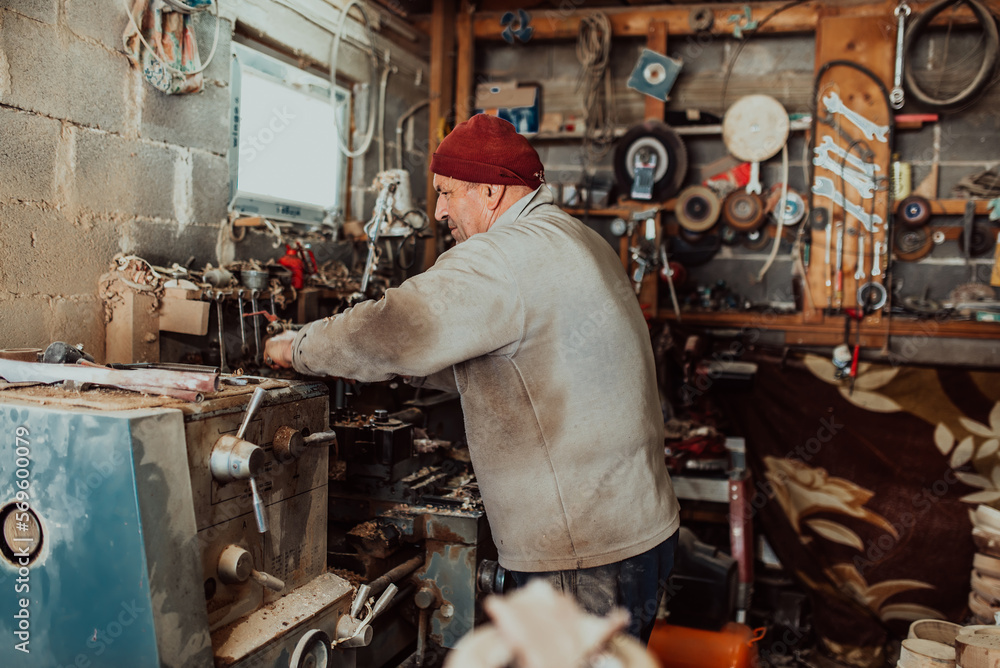 A senior man procesing wood on a lathe and making wooden dishes in the workshop A senior man procesing wood on a lathe and making wooden dishes in the workshop