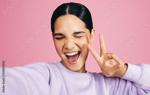 Excited woman taking a selfie and doing a peace sign in a studio photo