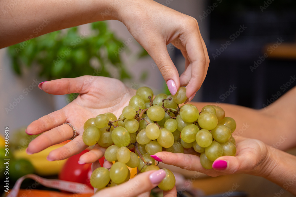 Fototapeta premium Close-up on the hands of two women handing each other a bunch of grapes