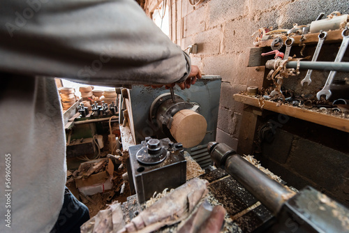 A senior man procesing wood on a lathe and making wooden dishes in the workshop photo