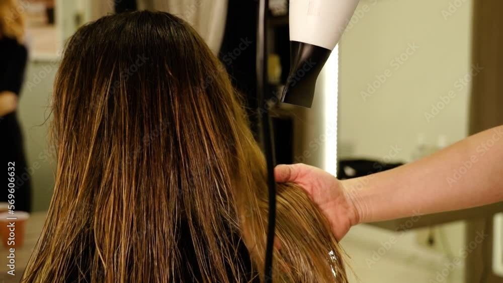 Careful master dries long brownish dyed hair of woman client using contemporary equipment in beauty salon closeup slow motion Careful master dries long brownish dyed hair of woman client using contemporary equipment in beauty salon closeup slow motion