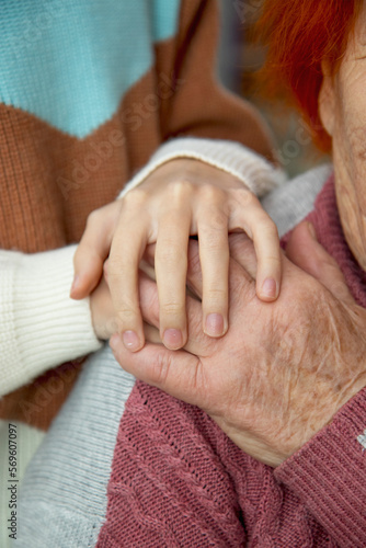 The hands of an old and a young woman embrace each other. Love and care for the older generation, respect for the elderly