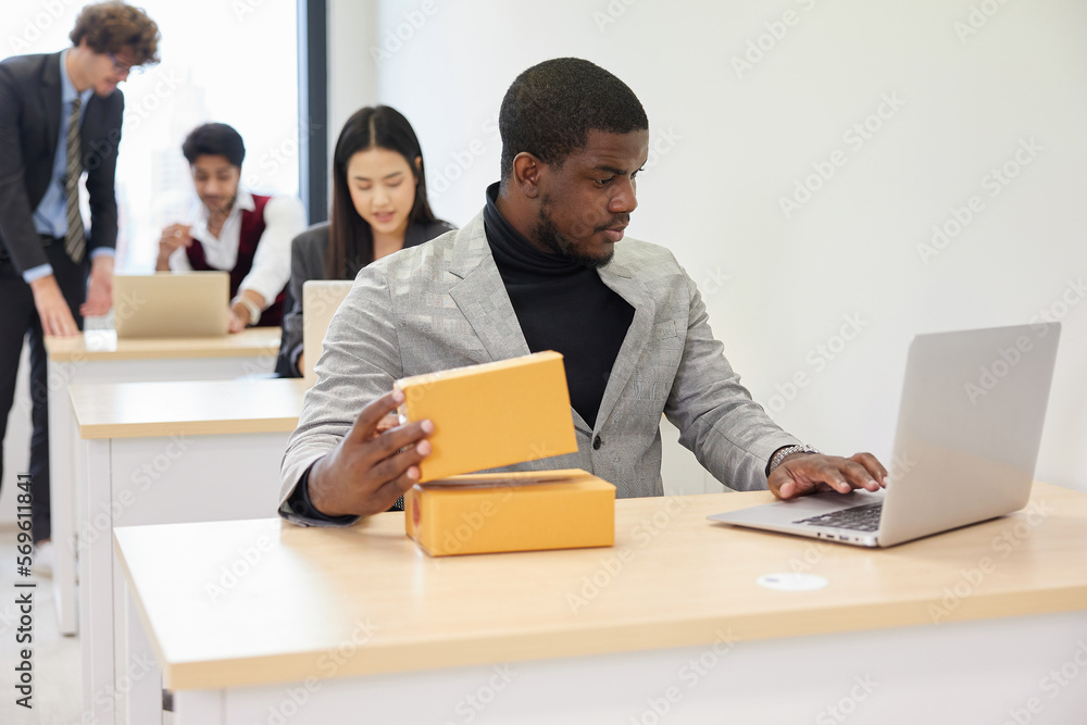 African businessman using laptop computer and checking parcel cardboard boxes from online shopping in the office African businessman using laptop computer and checking parcel cardboard boxes from online shopping in the office