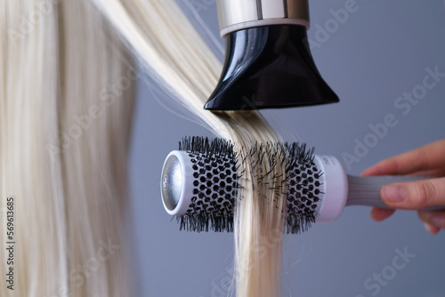 spa hair care concept. Drying blond hair with hair dryer and round brush.