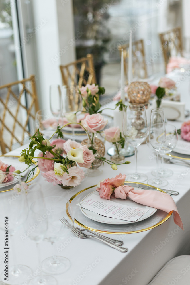 Fototapeta premium Wedding decorations. Served wedding table with decorative fresh pink flowers and candles. Celebration details. Flower composition roses plates and candles in candlesticks