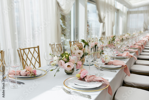 Wedding decorations. Served wedding table with decorative fresh pink flowers and candles. Celebration details. Flower composition roses plates and candles in candlesticks