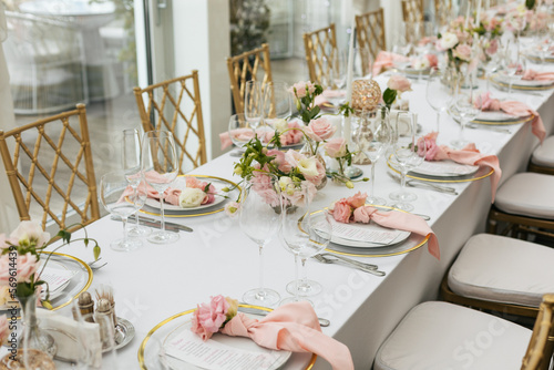 Wedding decorations. Served wedding table with decorative fresh pink flowers and candles. Celebration details. Flower composition roses plates and candles in candlesticks