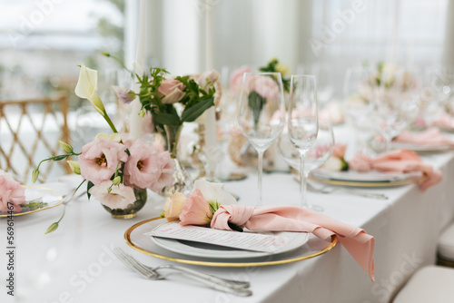 Wedding decorations. Served wedding table with decorative fresh pink flowers and candles. Celebration details. Flower composition roses plates and candles in candlesticks