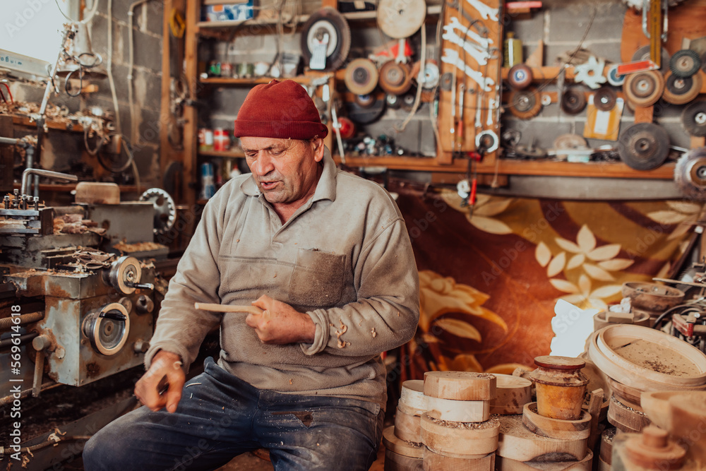A senior man sitting in the workshop and processing wooden utensils in the old manual way A senior man sitting in the workshop and processing wooden utensils in the old manual way