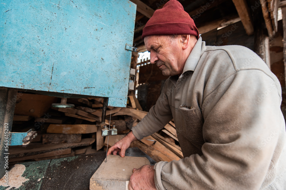 A senior man processing wood on a machine in an outdoor workshop. A senior man processing wood on a machine in an outdoor workshop.