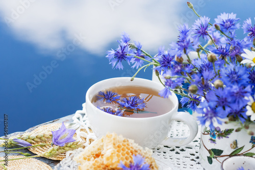 Photos Cornflower herbal tea in white cup on white crochet napkin on wooden table outdo