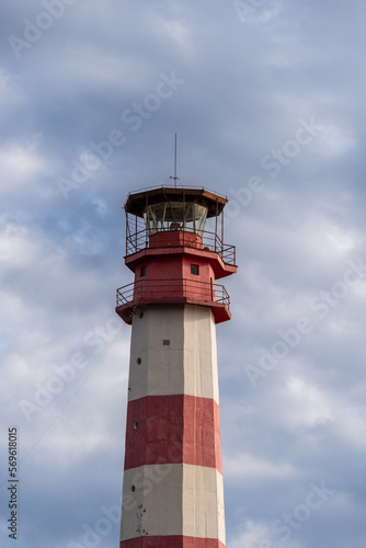 Modern lighthouse on thick cape. Gelendzhik. Multifaceted red and white column of lighthouse tower is 50 meters high against blue sky with white clouds. Close-up.