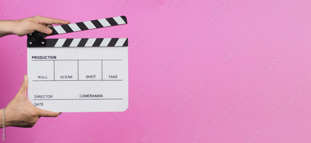 Hands are holding a clapper board or movie slate on pink background.