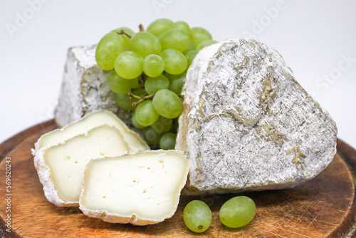 Assorted mouldy blue cheeses goat's milk on a wooden chopping board with green grapes. White background