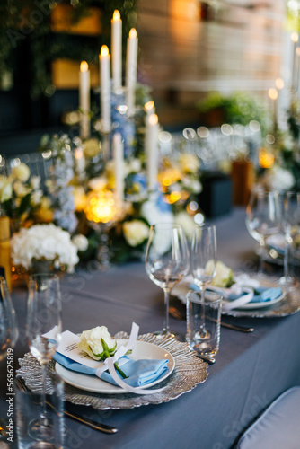 Close-up of a festive table setting. Silver plate decorated with a blue napkin and white natural roses on a gray tablecloth. Wedding decoration concept 