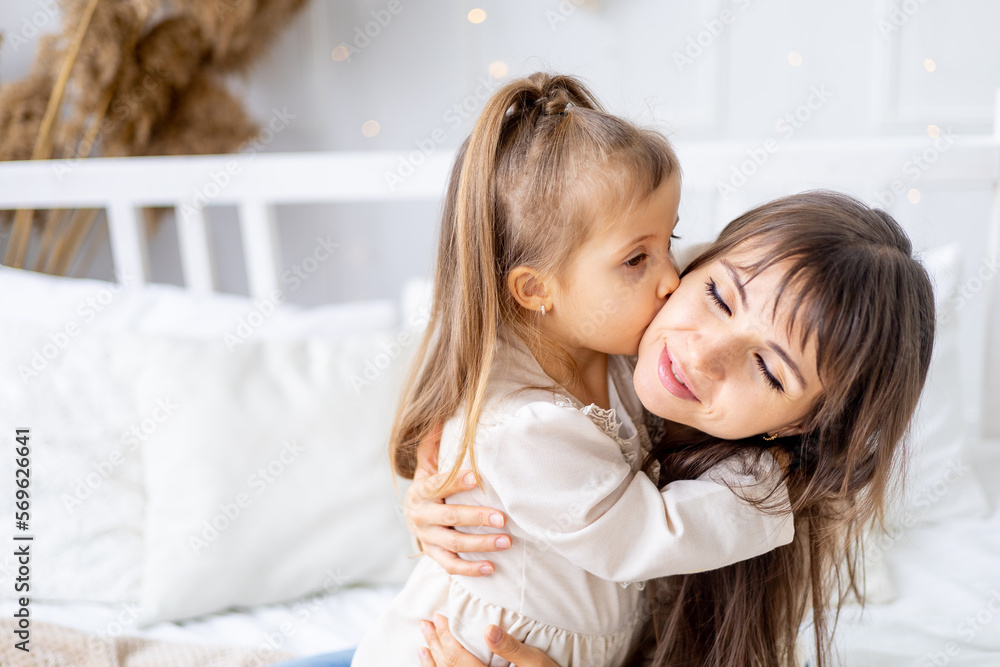 a little baby girl with her mom hugging and kissing at home on the bed. Lifestyle. Happy family and motherhood. International Women's Day or Mother's Day. High-quality photography a little baby girl with her mom hugging and kissing at home on the bed. Lifestyle. Happy family and motherhood. International Women's Day or Mother's Day. High-quality photography