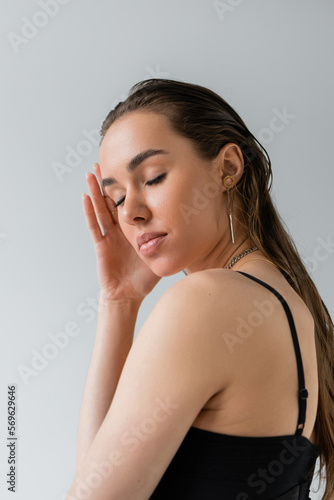 portrait of brunette woman in black top posing with closed eyes isolated on gray.
