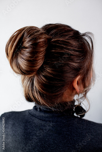  The back view of girl has an evening professional hairstyle made of her brunette hair. The woman is wearing hanging earrings