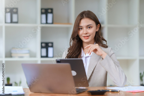 Pretty Asian businesswoman sitting smiling and happy working on laptop computer and document in office. Looking at camera.