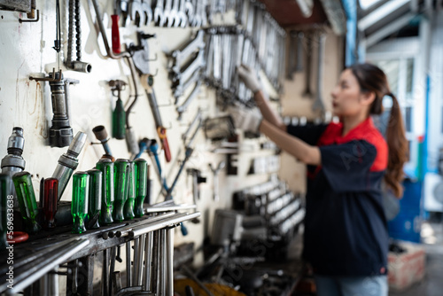 Selective focus of various car repair tools, screwdrivers, hanging on the wall and keep in toolholders in a garage with a blurred on right side of Asian female mechanic in uniform hanging tool on wall