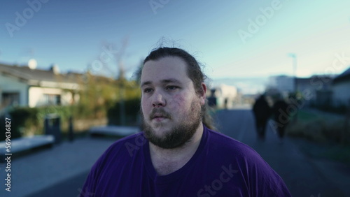 One pensive overweight young man walking outside in street in contemplation. A meditative young fat male person. Tracking shot