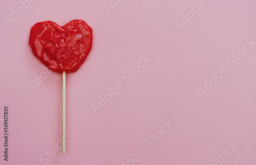 Red candy in the form of a heart on a stick on a pink background.
