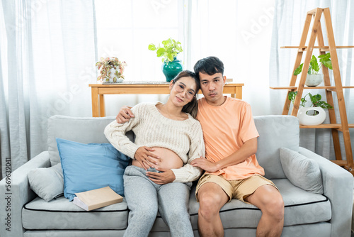 Asian couple. Pregnant wife sitting and talking. Pregnant woman sitting next to her reading a book on the sofa in the house.