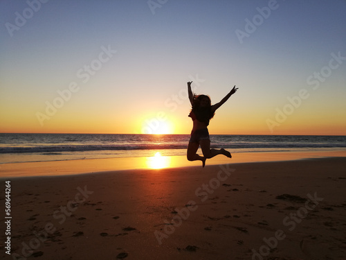 person jumping on the beach at sunset