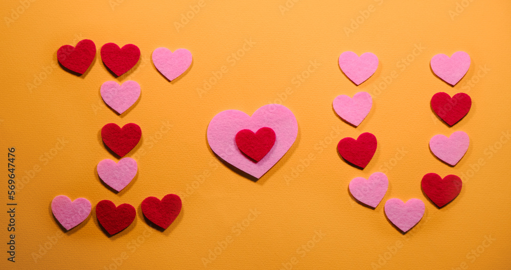 The inscription I love you is laid out on a yellow background of small pink and red hearts. View from above. The concept of Valentine's Day.