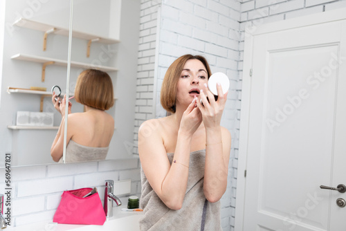 Attractive young woman putting on makeup after taking a shower in the bathroom 