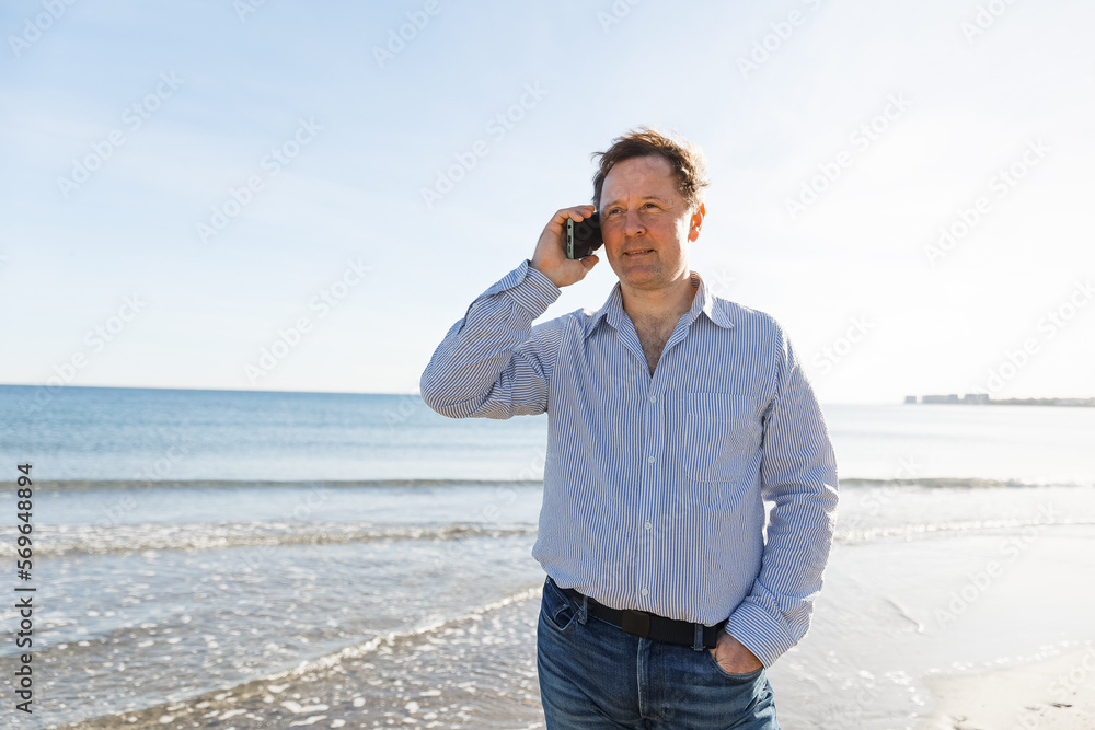 Businessman Talking On Phone, using smartphone mobile apps texting message, surfing social media tech standing on the city beach against the backdrop of the sea Businessman Talking On Phone, using smartphone mobile apps texting message, surfing social media tech standing on the city beach against the backdrop of the sea