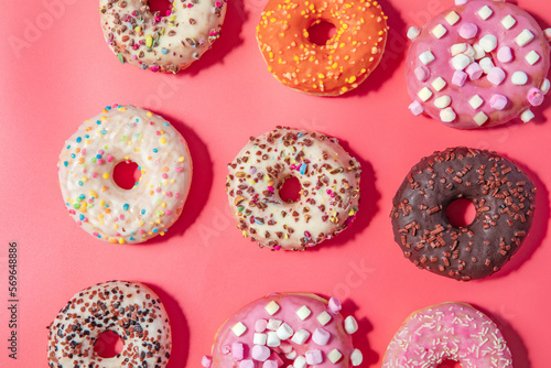 Donuts with icing on pastel pink background. Sweet donuts. top view assorted with various chocolate glazed and sprinkles, sugar sweets concept